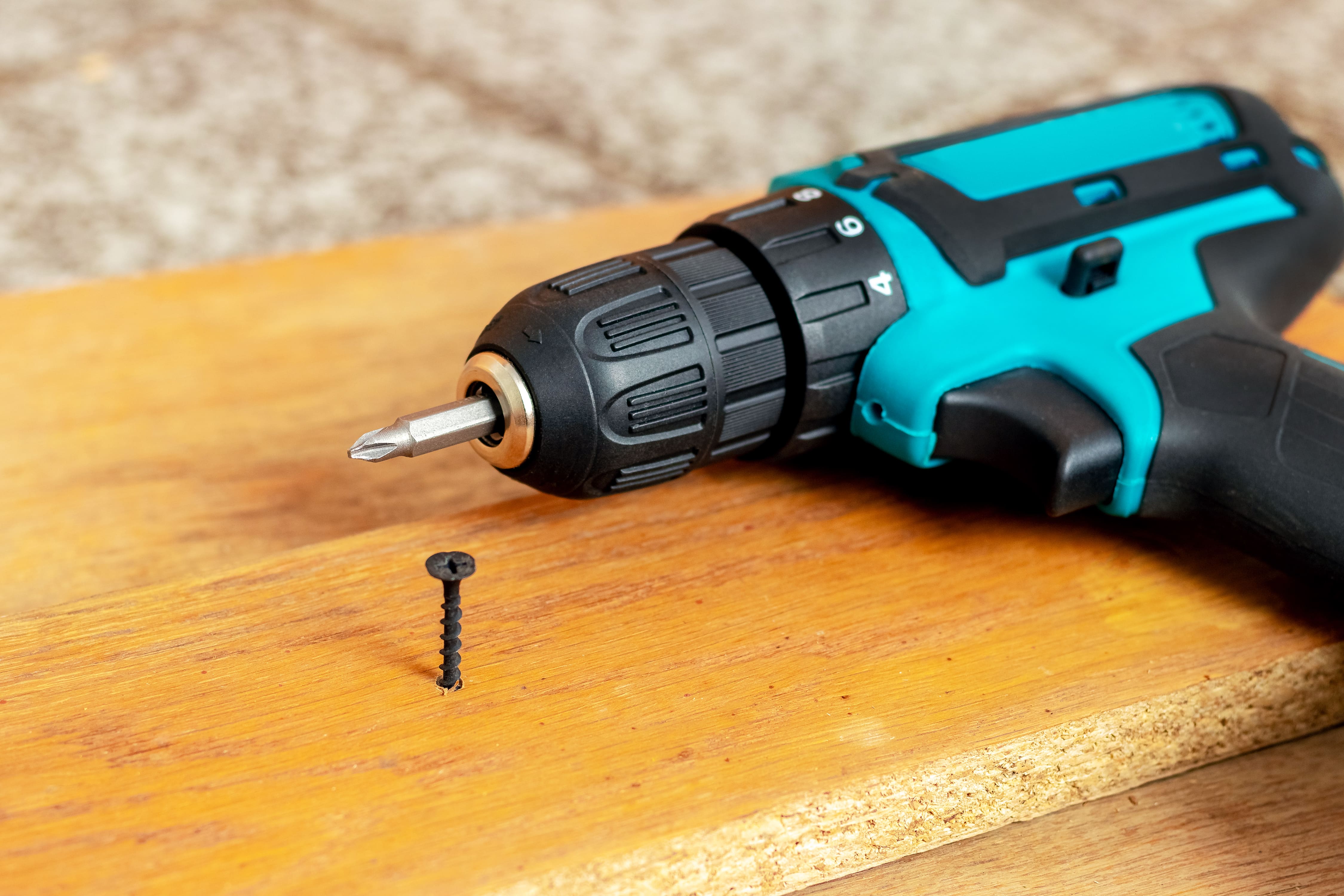 Electric screwdriver near a screw screwed into chipboard